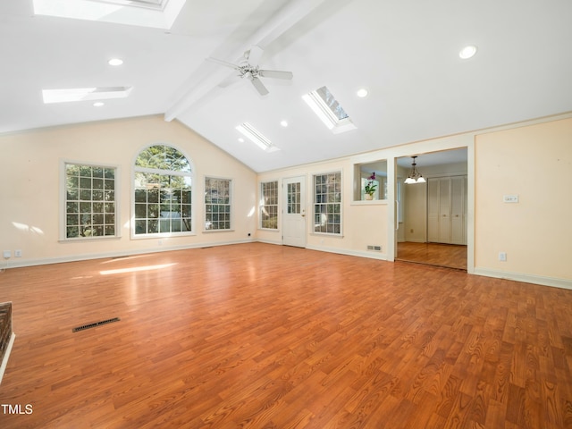 unfurnished living room with wood finished floors, baseboards, visible vents, vaulted ceiling with skylight, and ceiling fan