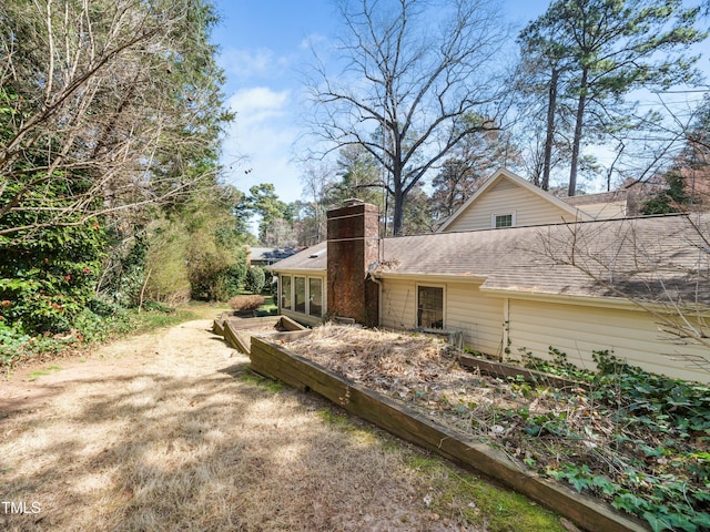 rear view of house with roof with shingles, a sunroom, and a chimney