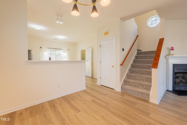 unfurnished living room with baseboards, light wood-style floors, a fireplace, and stairs