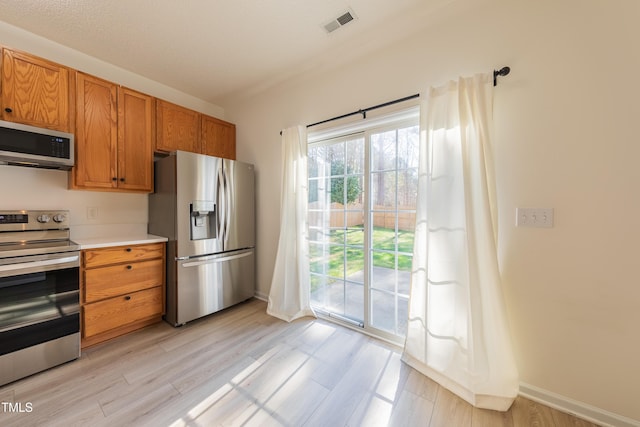 kitchen featuring stainless steel appliances, light wood finished floors, brown cabinetry, and light countertops