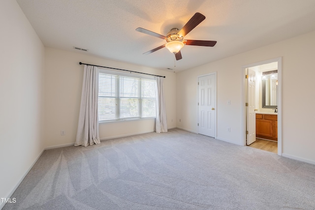 unfurnished bedroom featuring visible vents, baseboards, light colored carpet, ensuite bath, and a ceiling fan