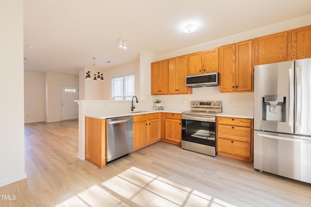 kitchen with light countertops, a peninsula, light wood-style floors, stainless steel appliances, and a sink