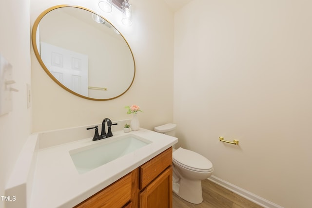 half bath featuring baseboards, toilet, wood finished floors, and vanity