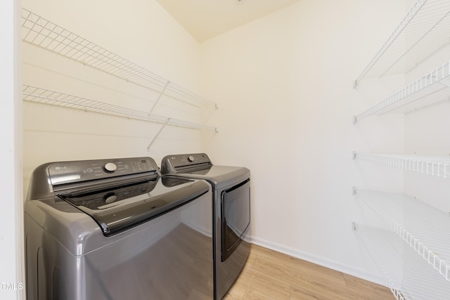 washroom featuring laundry area, washer and dryer, light wood-type flooring, and baseboards