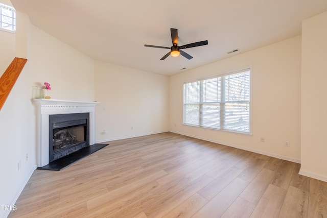 unfurnished living room featuring ceiling fan, baseboards, light wood-style floors, and a fireplace with raised hearth