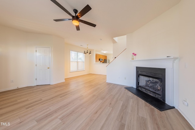 unfurnished living room featuring baseboards, light wood-style floors, a fireplace with raised hearth, and ceiling fan with notable chandelier