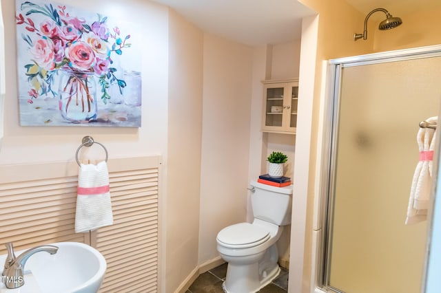 bathroom featuring baseboards, a stall shower, a sink, tile patterned flooring, and toilet