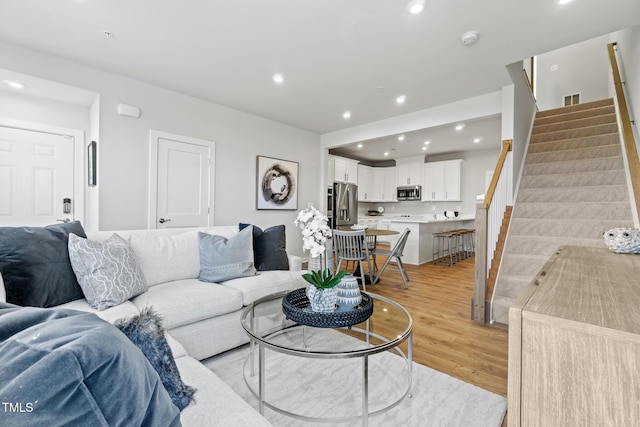 living area with light wood finished floors, visible vents, recessed lighting, and stairs