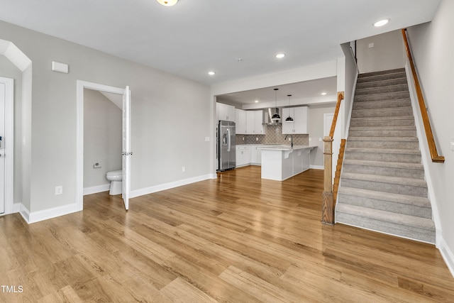 unfurnished living room featuring stairway, recessed lighting, baseboards, and light wood-style floors