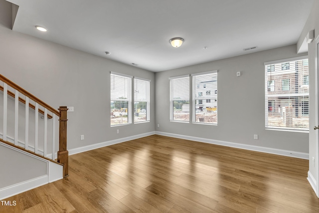 unfurnished living room with stairs, wood finished floors, visible vents, and baseboards