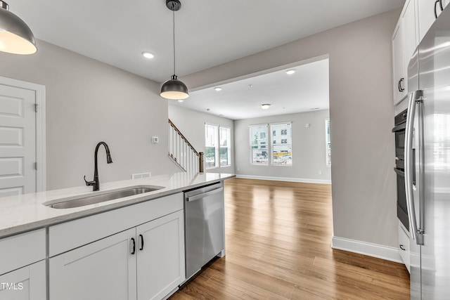 kitchen with appliances with stainless steel finishes, white cabinetry, light wood-style floors, and a sink