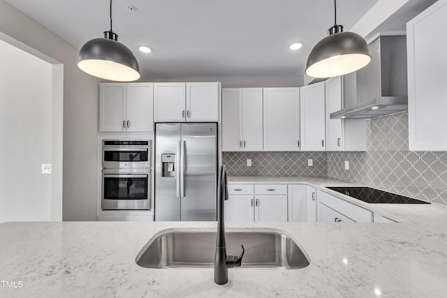 kitchen with light stone counters, appliances with stainless steel finishes, white cabinets, wall chimney range hood, and decorative backsplash