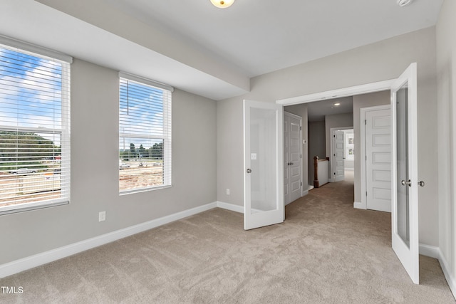 unfurnished bedroom featuring french doors, baseboards, and light carpet