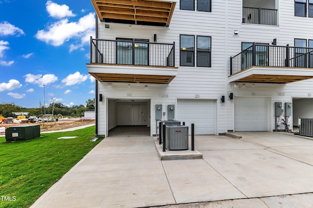 rear view of house with driveway, a lawn, central AC, and an attached garage