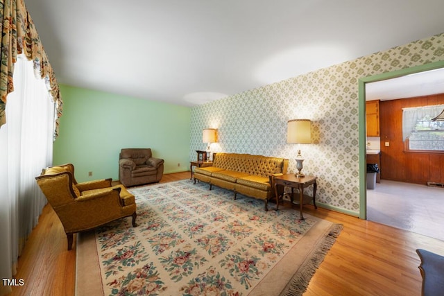 living area with wallpapered walls, light wood-style floors, and baseboards