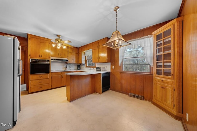 kitchen featuring under cabinet range hood, a peninsula, black appliances, and brown cabinetry