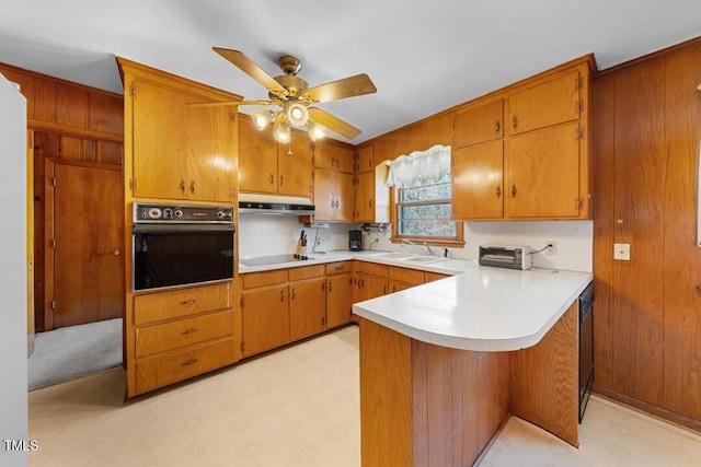 kitchen featuring light floors, a peninsula, a sink, black appliances, and under cabinet range hood