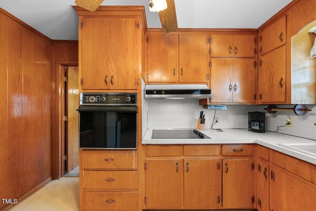 kitchen featuring under cabinet range hood, light countertops, brown cabinets, black appliances, and a sink