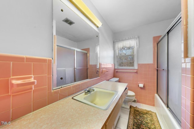 full bath featuring tile patterned flooring, visible vents, a wainscoted wall, toilet, and tile walls