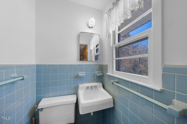 bathroom with wainscoting, toilet, and tile walls