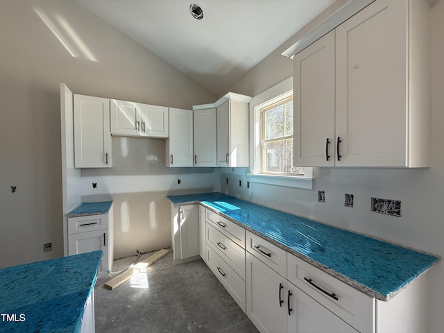 kitchen featuring white cabinets, stone countertops, concrete floors, and lofted ceiling