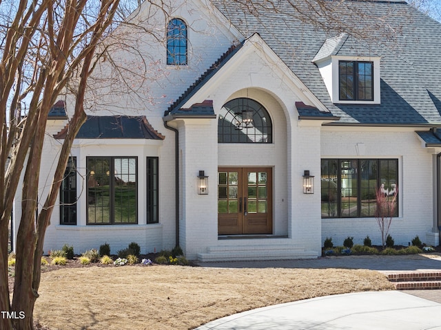 property entrance featuring brick siding, french doors, and a shingled roof