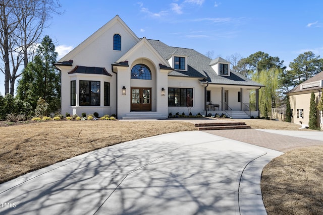 view of front facade featuring decorative driveway, brick siding, covered porch, and roof with shingles