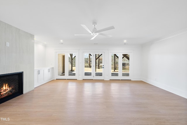 unfurnished living room with a large fireplace, light wood-style floors, crown molding, baseboards, and ceiling fan