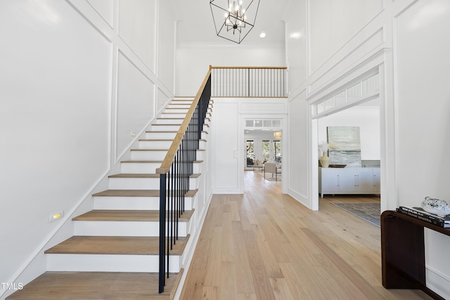 staircase featuring a high ceiling, an inviting chandelier, wood finished floors, and crown molding