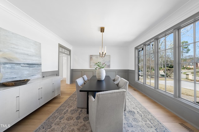 dining area featuring visible vents, light wood-style flooring, an inviting chandelier, wainscoting, and crown molding