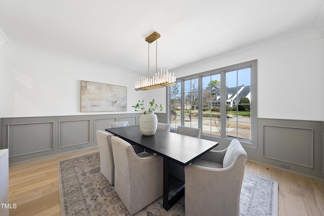 dining space featuring crown molding, a decorative wall, light wood finished floors, and wainscoting