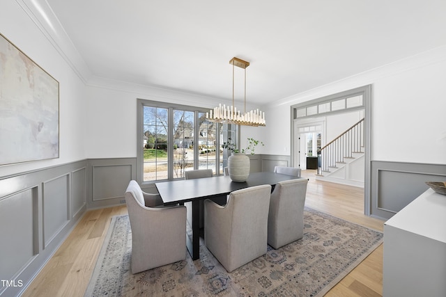 dining space featuring an inviting chandelier, crown molding, a decorative wall, and light wood-style floors