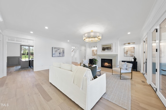 living room featuring a warm lit fireplace, light wood-type flooring, and ornamental molding