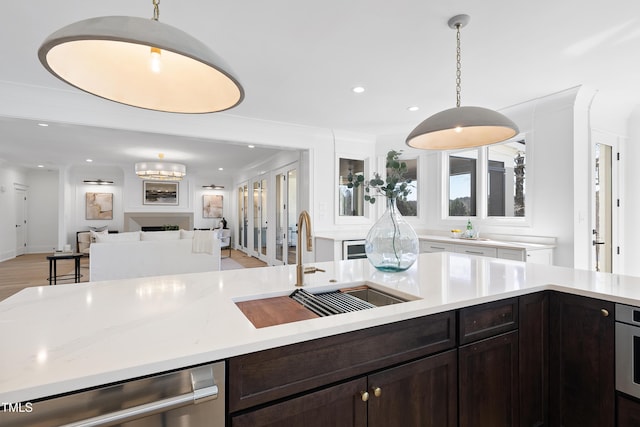 kitchen with a sink, dark brown cabinets, appliances with stainless steel finishes, decorative light fixtures, and open floor plan