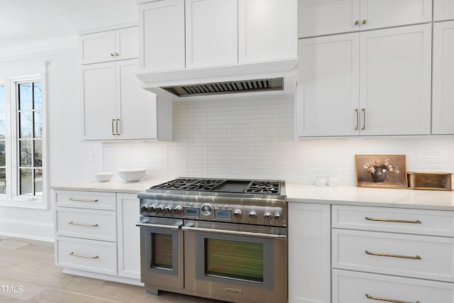 kitchen featuring premium range hood, double oven range, white cabinetry, light countertops, and decorative backsplash