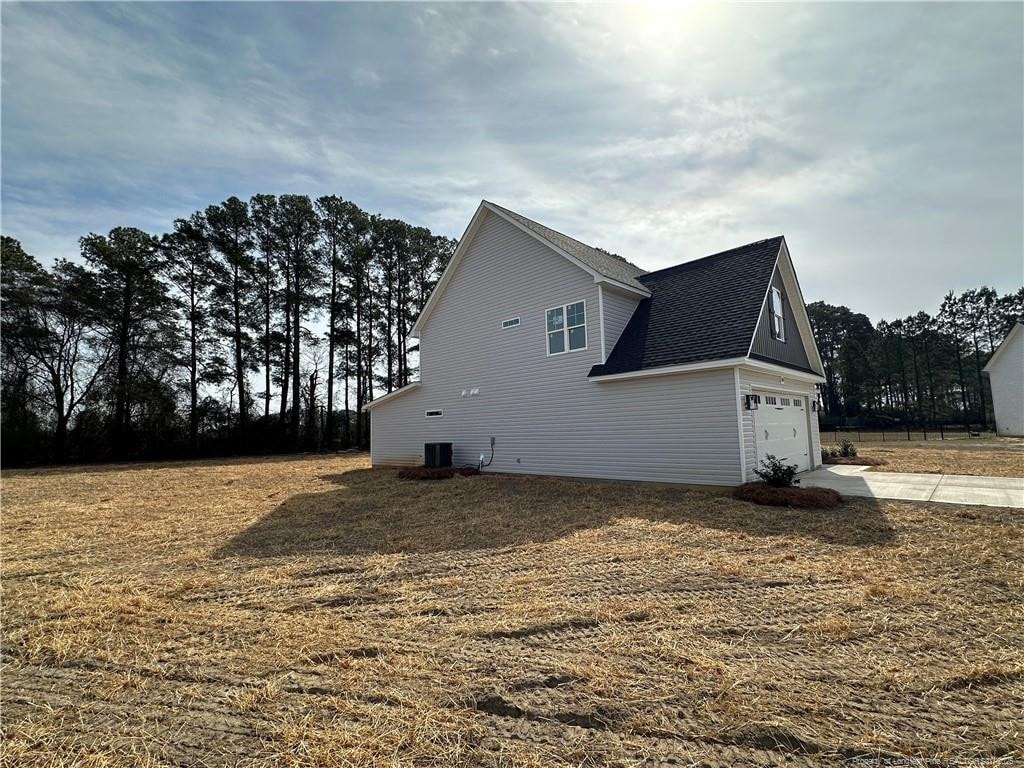 view of property exterior with central air condition unit, an attached garage, driveway, and roof with shingles