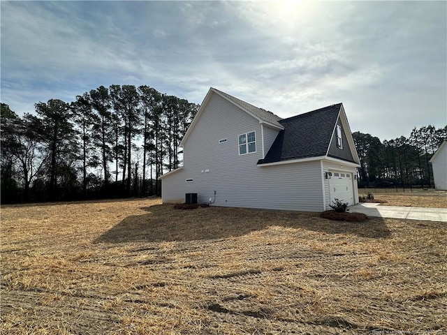 view of property exterior with central air condition unit, an attached garage, driveway, and roof with shingles