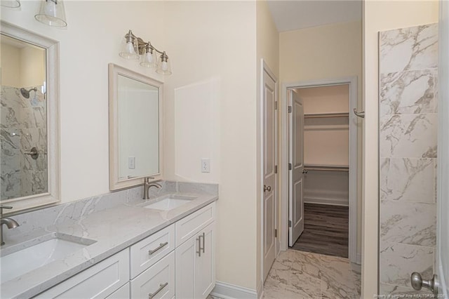bathroom with double vanity, a walk in closet, marble finish floor, and a sink