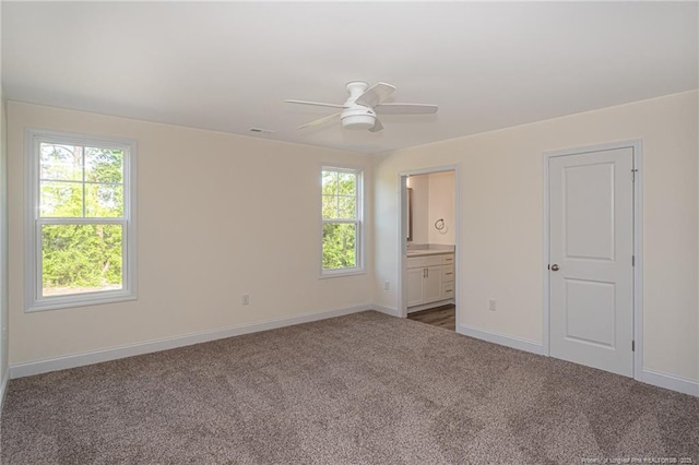 unfurnished bedroom featuring carpet, baseboards, ensuite bath, and multiple windows