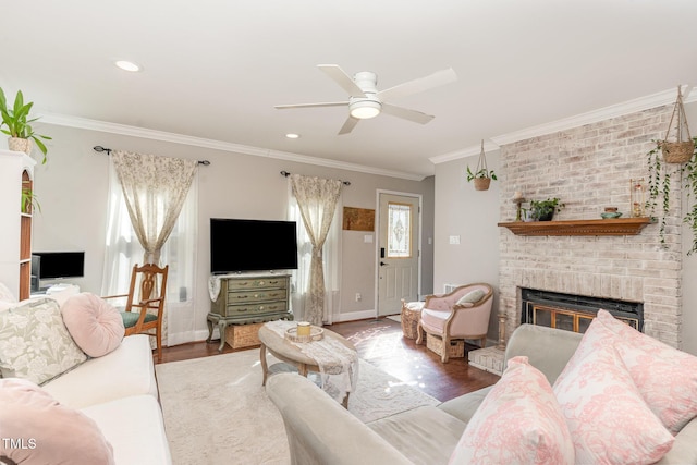 living room with a brick fireplace, crown molding, ceiling fan, baseboards, and wood finished floors