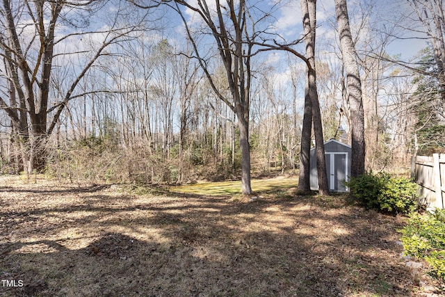 view of yard with a storage unit, an outdoor structure, a wooded view, and fence