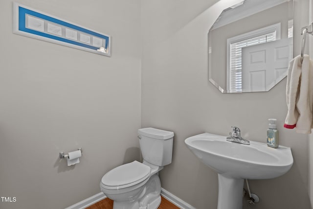 half bathroom featuring toilet, wood finished floors, and baseboards