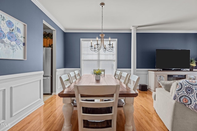 dining area featuring light wood-type flooring, a wainscoted wall, a chandelier, and ornamental molding