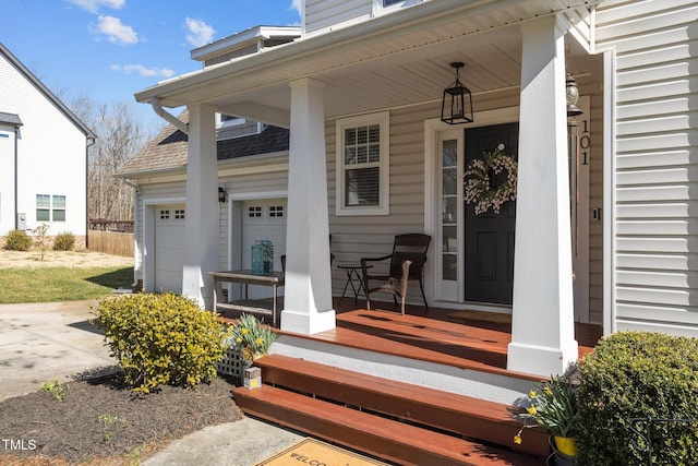 view of exterior entry with driveway, a garage, covered porch, and roof with shingles