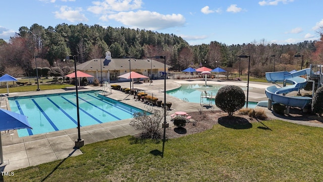 pool with a patio area, a forest view, a water slide, and a yard