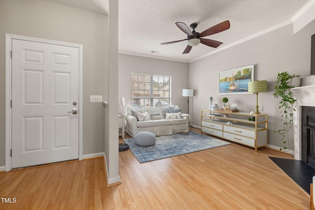 living area with a fireplace with flush hearth, a textured ceiling, wood finished floors, crown molding, and ceiling fan