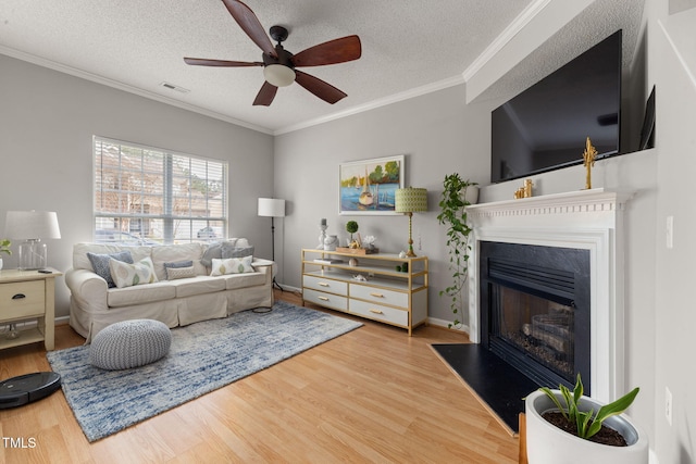 living room featuring a ceiling fan, wood finished floors, visible vents, and a textured ceiling