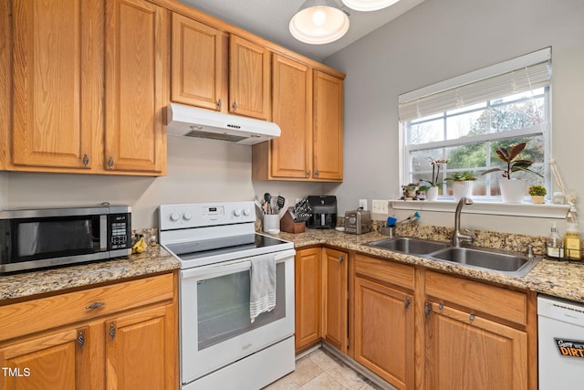 kitchen with white appliances, brown cabinetry, light stone countertops, a sink, and under cabinet range hood