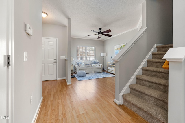 foyer entrance featuring stairway, light wood finished floors, ornamental molding, ceiling fan, and a textured ceiling