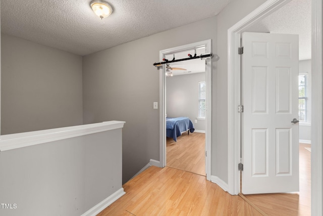 hall with light wood-type flooring, baseboards, a textured ceiling, and an upstairs landing